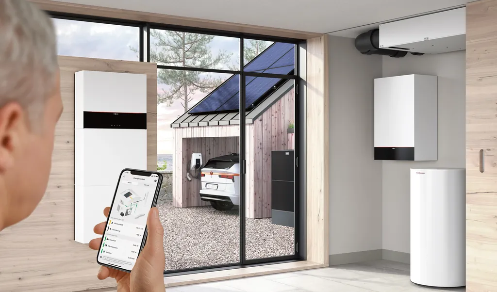 Viessmann ViCare app on a smartphone, with an indoor heat pump unit, a battery storage system and an electric car charging under a solar carport